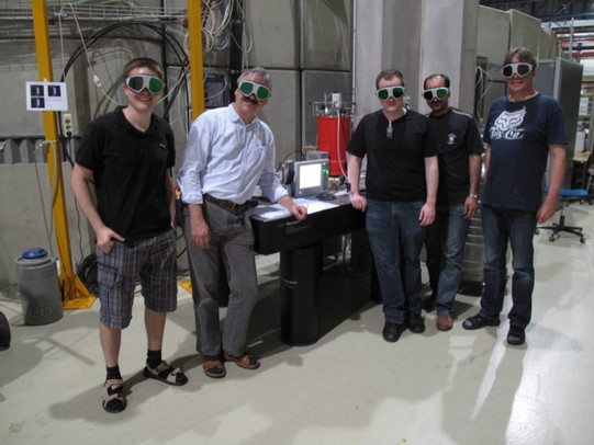 Fünf Personen mit Laserschutzbrillen stehen vor einem optischen Tisch in der DELTA-Halle. Das Bild wurde anlässlich der ersten Laser-Elektronen-Wechselwirkung aufgenommen.