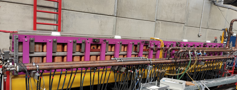 In der Mitte des Bildes sind die Magnete des Undulator U250 in ihrer lila Halterung zu sehen. Im Hintergrund sieht man die Betonmauer und im Vordergrund eine Kabelpritsche.